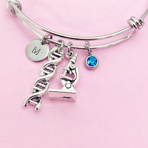 May include: A silver charm bracelet with a blue crystal charm, a DNA double helix charm, and a microscope charm. The bracelet also has a silver charm with the letter "M" on it.