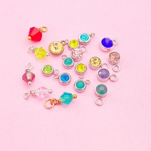 May include: Assortment of colorful rhinestone charms with silver and gold accents. The charms feature various colors including red, blue, green, yellow, pink, and clear.