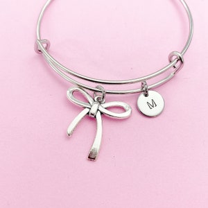 May include: A silver bangle bracelet with a silver bow charm and a silver charm with the letter "M" engraved on it.