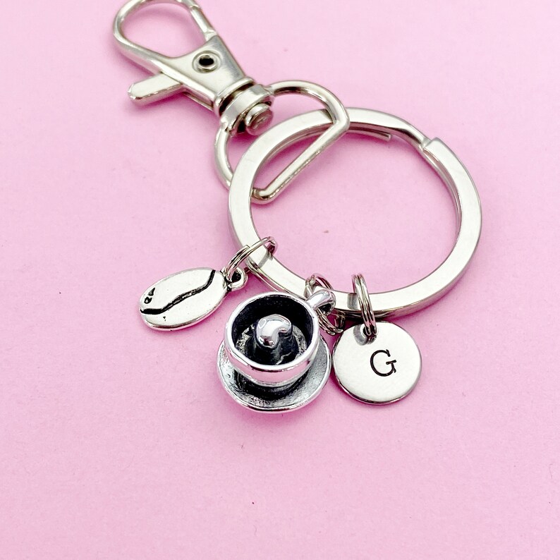 May include: Silver keychain with a coffee cup charm, a coffee bean charm, and a charm with the letter "G" on it.