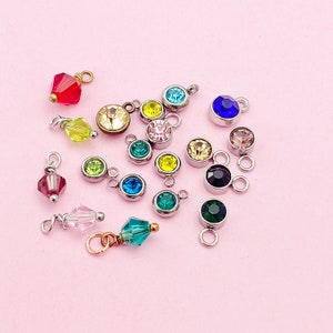 May include: Assortment of colorful crystal charms with silver and gold accents. The charms feature various shapes and sizes of crystals, including round, square, and teardrop.