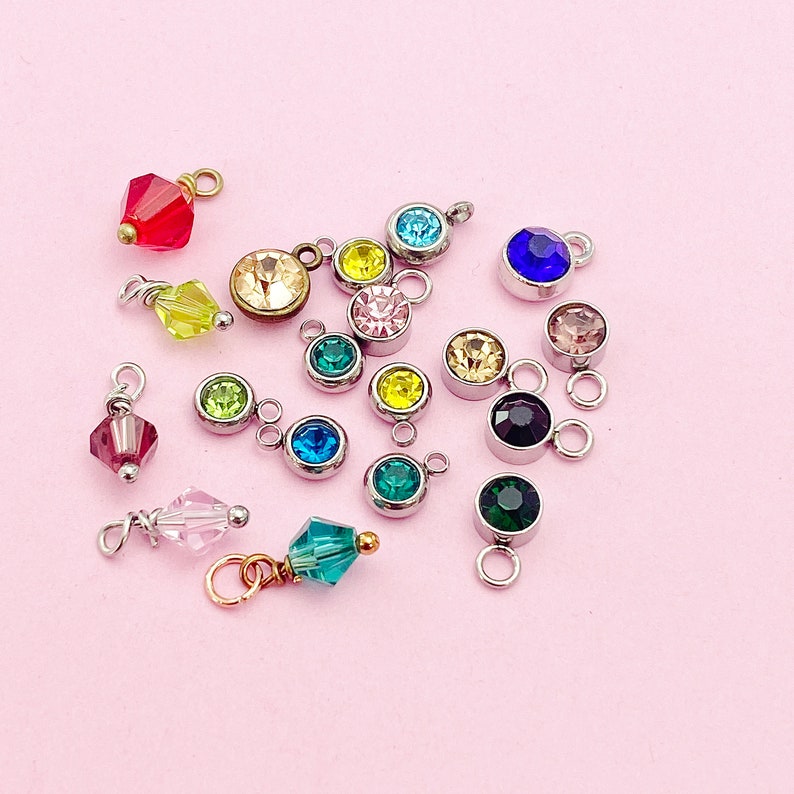 May include: Assortment of colorful crystal charms with silver and gold accents. The charms feature various shapes and sizes of crystals, including round, square, and teardrop.