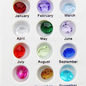 May include: A chart of twelve birthstones, one for each month of the year. The stones are arranged in rows of three, with the months labeled below each stone. The stones are red, purple, light blue, clear, green, lavender, red, light green, blue, pink, brown, and turquoise.