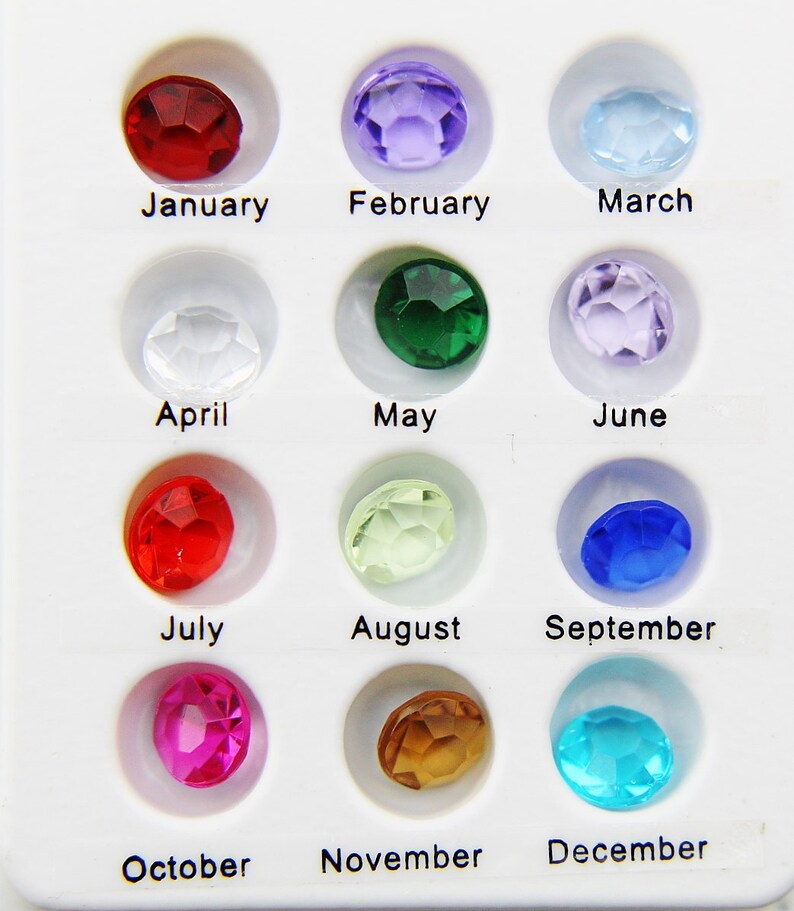 May include: A chart of twelve birthstones, one for each month of the year. The stones are arranged in rows of three, with the months labeled below each stone. The stones are red, purple, light blue, clear, green, lavender, red, light green, blue, pink, brown, and turquoise.