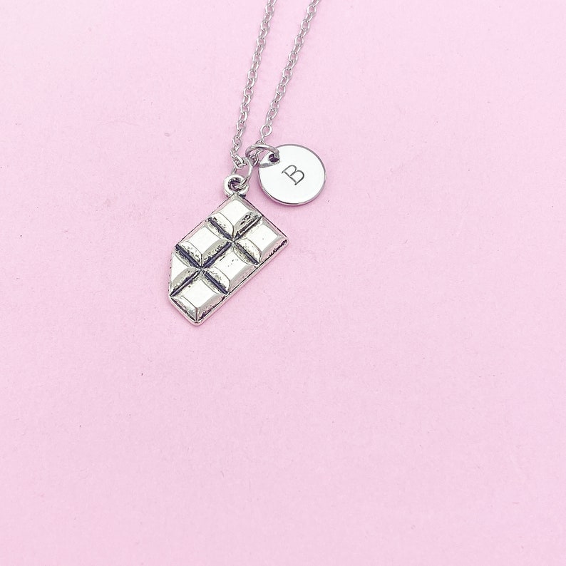 May include: Silver necklace with a chocolate bar charm and a round charm with the letter "B" on it.