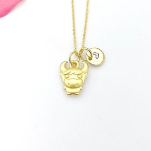 May include: Gold necklace with a small bull charm and a heart charm. The necklace is on a white background.