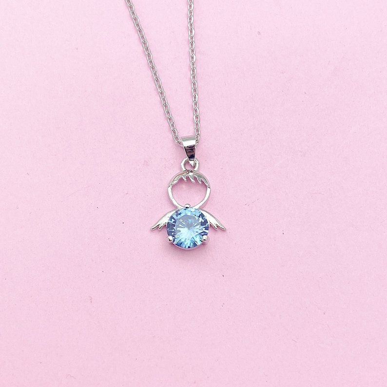 May include: A silver necklace with a blue crystal pendant shaped like an angel with outstretched wings.