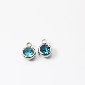 May include: Two silver charms with a blue gemstone in the center. The charms have a loop at the top for attaching to a bracelet or necklace.