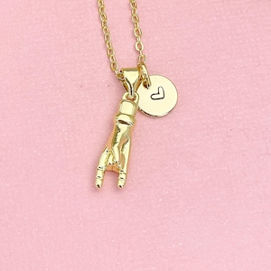 May include: A gold-toned necklace featuring a pendant shaped like a hand making a rock-and-roll gesture, accompanied by a small, round, flat charm engraved with a simple black outline of a heart. The chain is a delicate link style in gold.