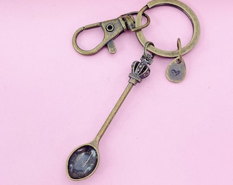 May include: A gold-toned spoon keychain with a crown charm and a heart-shaped charm. The keychain is attached to a silver-toned metal ring.
