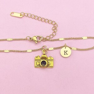 May include: Gold chain bracelet with a camera charm and a charm with the letter K.