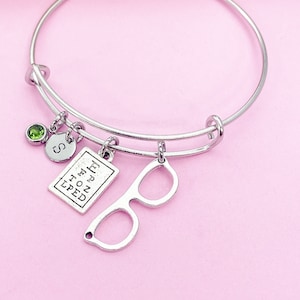 May include: Silver charm bracelet with a green stone charm, a charm with the letter "S", a charm with the text "Lived to tell the tale", and a charm shaped like a pair of glasses.