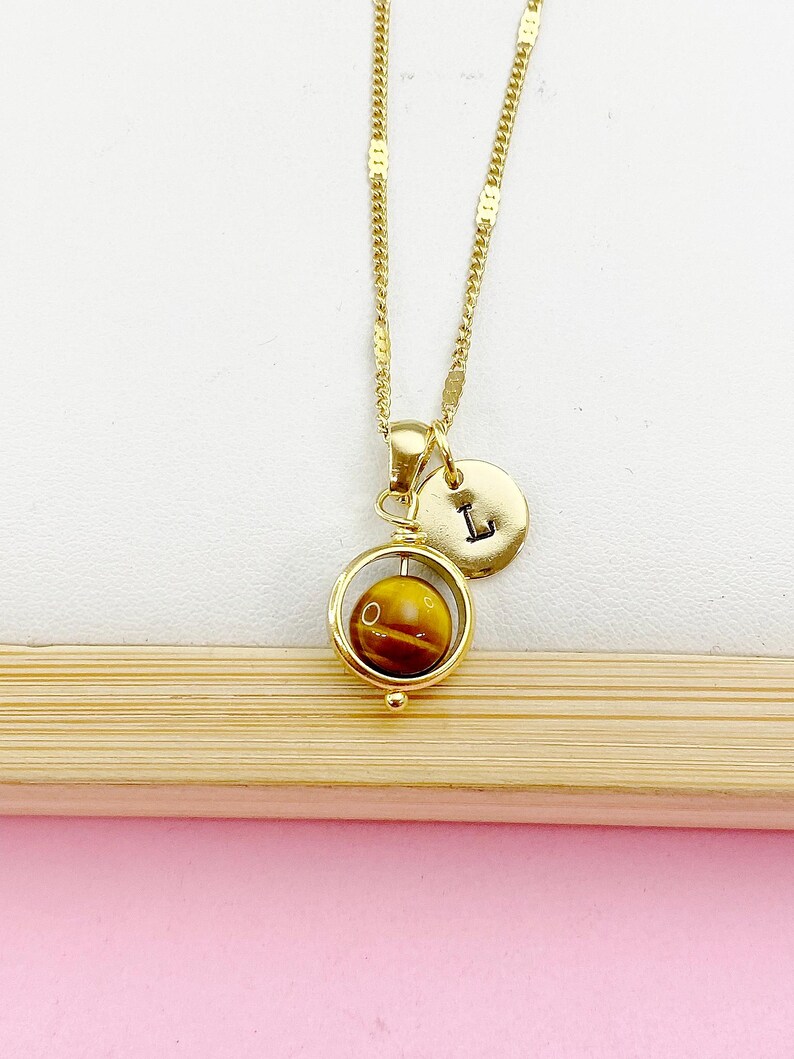 May include: Gold necklace with a spinning tiger's eye stone pendant and a gold initial charm with the letter "L".