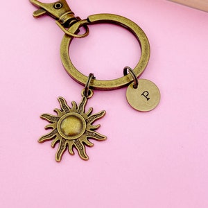 May include: A gold-toned keychain with a sun charm and a round charm with the letter "P" engraved on it. The keychain is attached to a split ring.