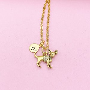 May include: Gold necklace with a small chihuahua charm and a round charm with the letter D. The necklace is on a pink background.