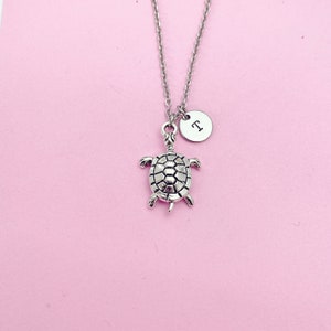 May include: Silver turtle necklace with a silver charm that says "T" on a pink background.