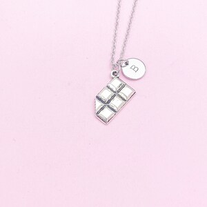 May include: Silver necklace with a chocolate bar charm and a small round charm with the letter "B" on it.