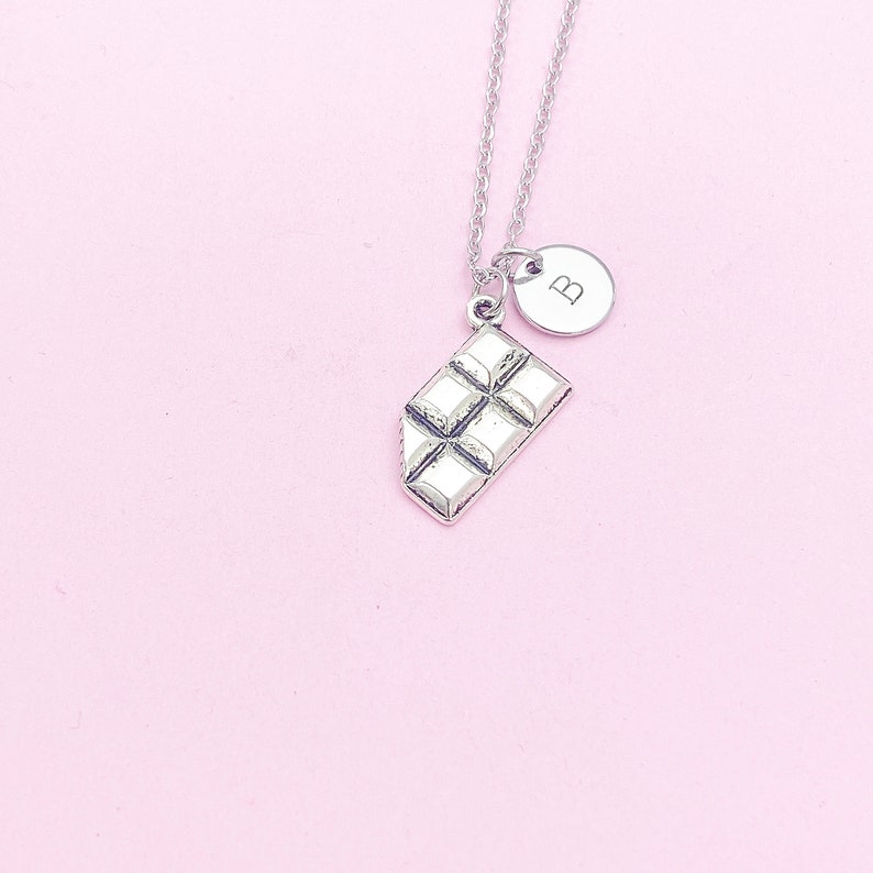 May include: Silver necklace with a chocolate bar charm and a small round charm with the letter "B" on it.