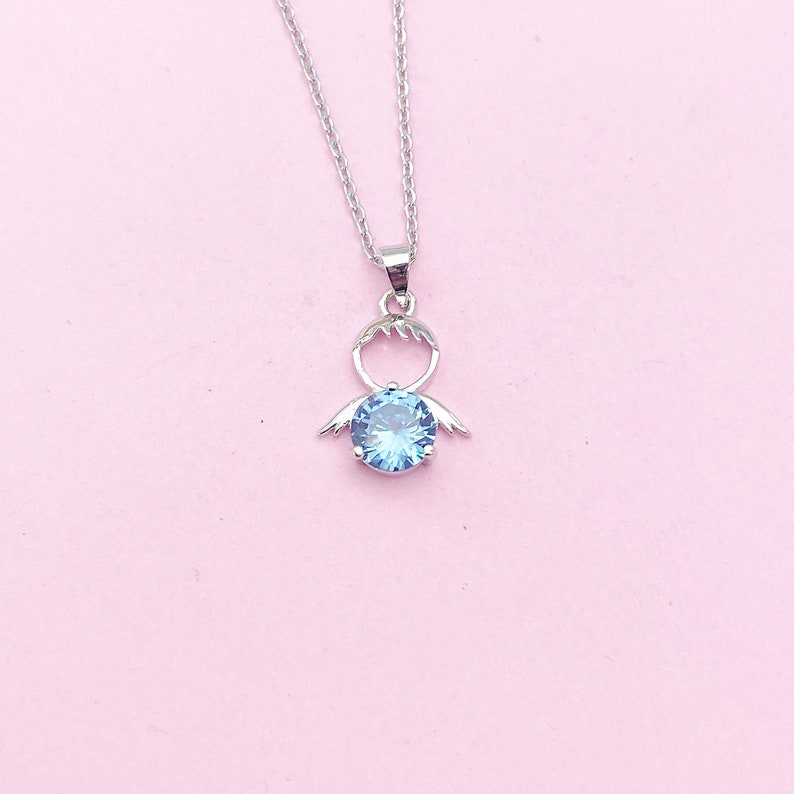 May include: A silver necklace with a blue crystal pendant shaped like an angel with wings.