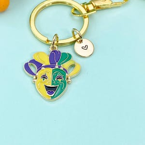 May include: A gold-colored keychain featuring a Mardi Gras jester mask charm with yellow, green, purple, and gold accents. A small round charm with a heart is also attached.