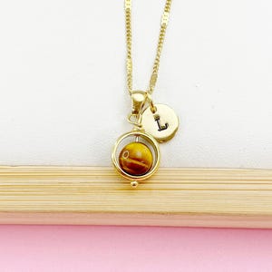 May include: Gold necklace with a spinning tiger's eye stone pendant and a gold charm with the letter 'L'.