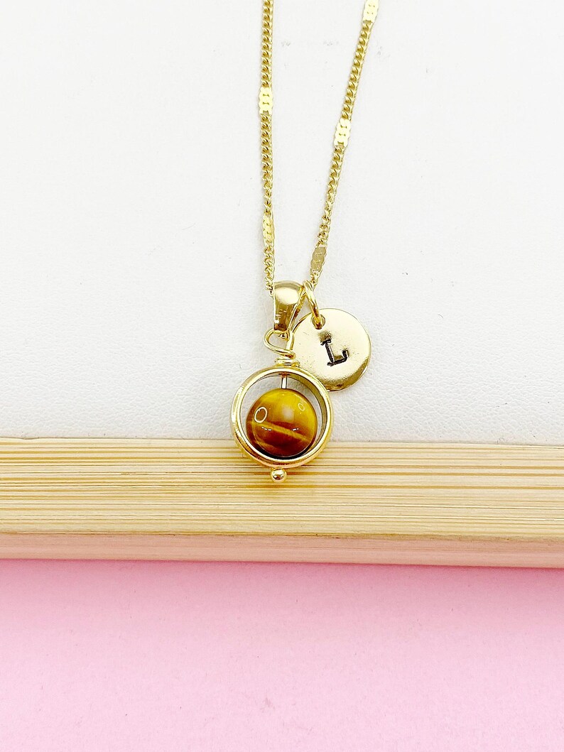May include: Gold necklace with a spinning tiger's eye stone pendant and a gold charm with the letter 'L'.