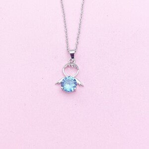 May include: A silver necklace with a pendant featuring a blue gemstone and a stylized angel wing design.