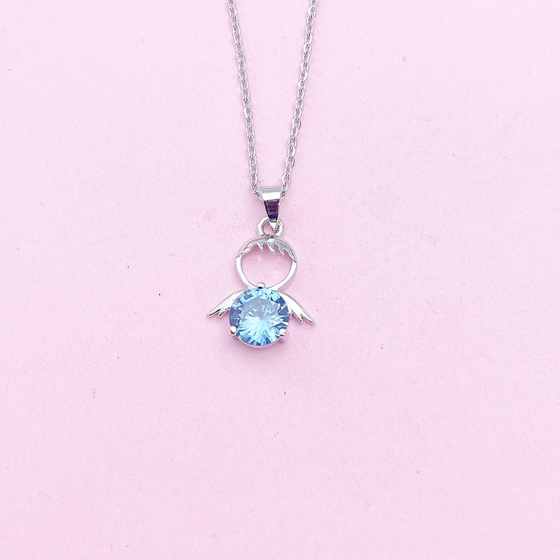 May include: A silver necklace with a pendant featuring a blue gemstone and a stylized angel wing design.