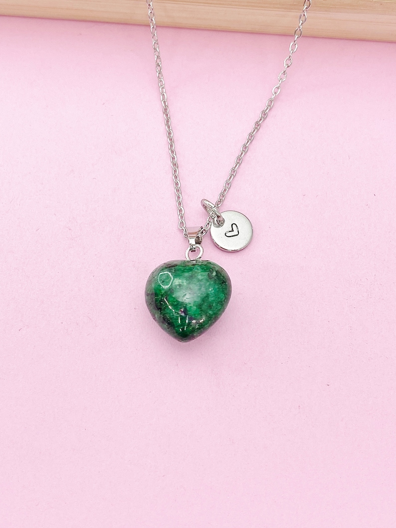 May include: A silver chain necklace with a green heart-shaped pendant and a small silver charm with a heart symbol.