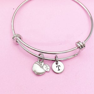 May include: Silver bangle bracelet with an apple charm and a charm with the letter T.