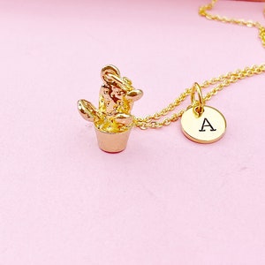 May include: Gold necklace with a small cactus charm and a round pendant with the letter 'A' on it.