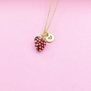 May include: A gold chain necklace with a red and green strawberry charm and a small gold heart charm.