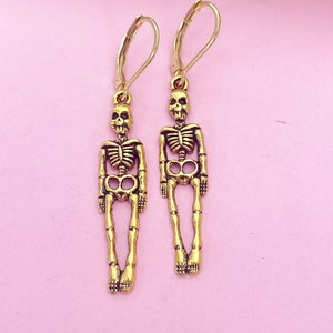 May include: A pair of gold skeleton earrings with a dangling skeleton charm. The earrings have a hook closure.