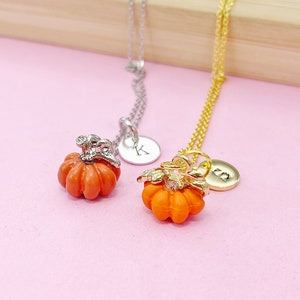May include: Two gold necklaces with pumpkin charms. One necklace has a silver chain and a letter "K" charm. The other necklace has a gold chain and a letter "S" charm.