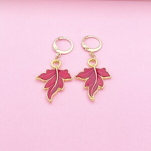 May include: A pair of gold earrings with red leaf-shaped charms. The leaves have a detailed design and are accented with gold.