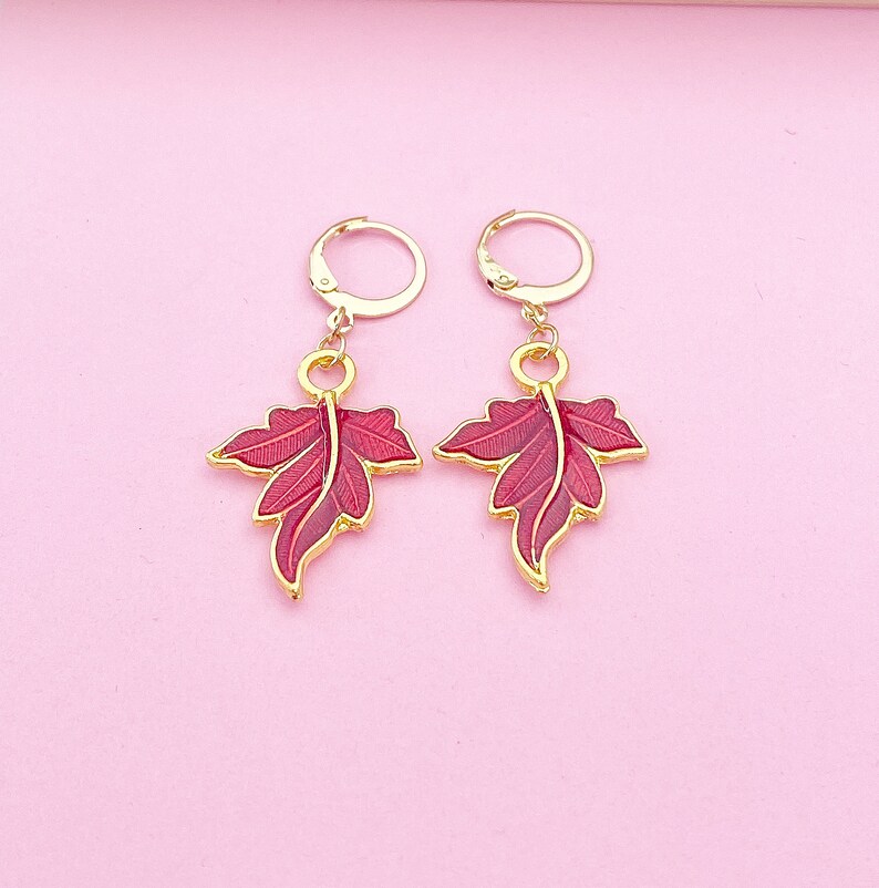 May include: A pair of gold earrings with red leaf-shaped charms. The leaves have a detailed design and are accented with gold.
