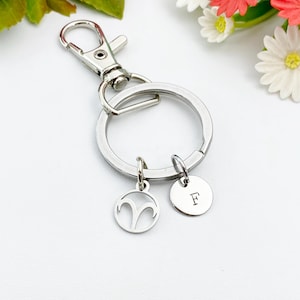 May include: Silver keychain with a silver charm featuring the astrological symbol for Aries and a silver charm with the letter F.