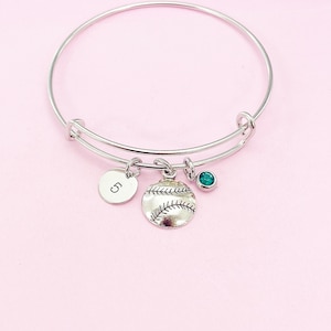May include: Silver bangle bracelet with a charm of a baseball, a round charm with the letter "C" and a green gemstone.