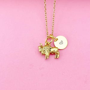 May include: A gold necklace with a small buffalo charm and a heart charm. The necklace is on a pink background.