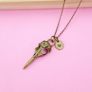May include: A gold-toned necklace with a bird skull pendant and a small heart charm. The pendant is detailed with floral accents.