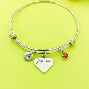 May include: A silver bangle bracelet with a heart charm engraved with the word "jammma" and a small red rhinestone charm.