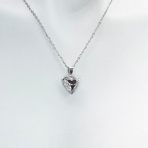 May include: A silver chain necklace with a heart-shaped locket pendant. The locket has a detailed, ornate design.