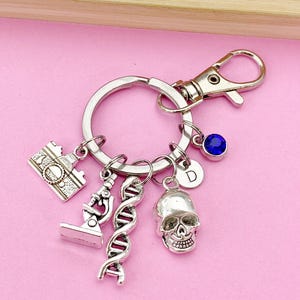 May include: Silver keychain with a skull charm, a microscope charm, a DNA charm, a building charm, a letter D charm, and a blue crystal charm.