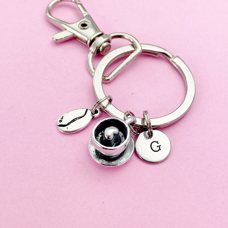 May include: Silver keychain with a coffee cup charm, a coffee bean charm, and a charm with the letter G. The keychain is attached to a silver key ring.
