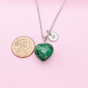May include: A silver chain necklace with a green heart-shaped pendant and a small silver charm with a heart engraved on it. The pendant is about the size of a US penny.