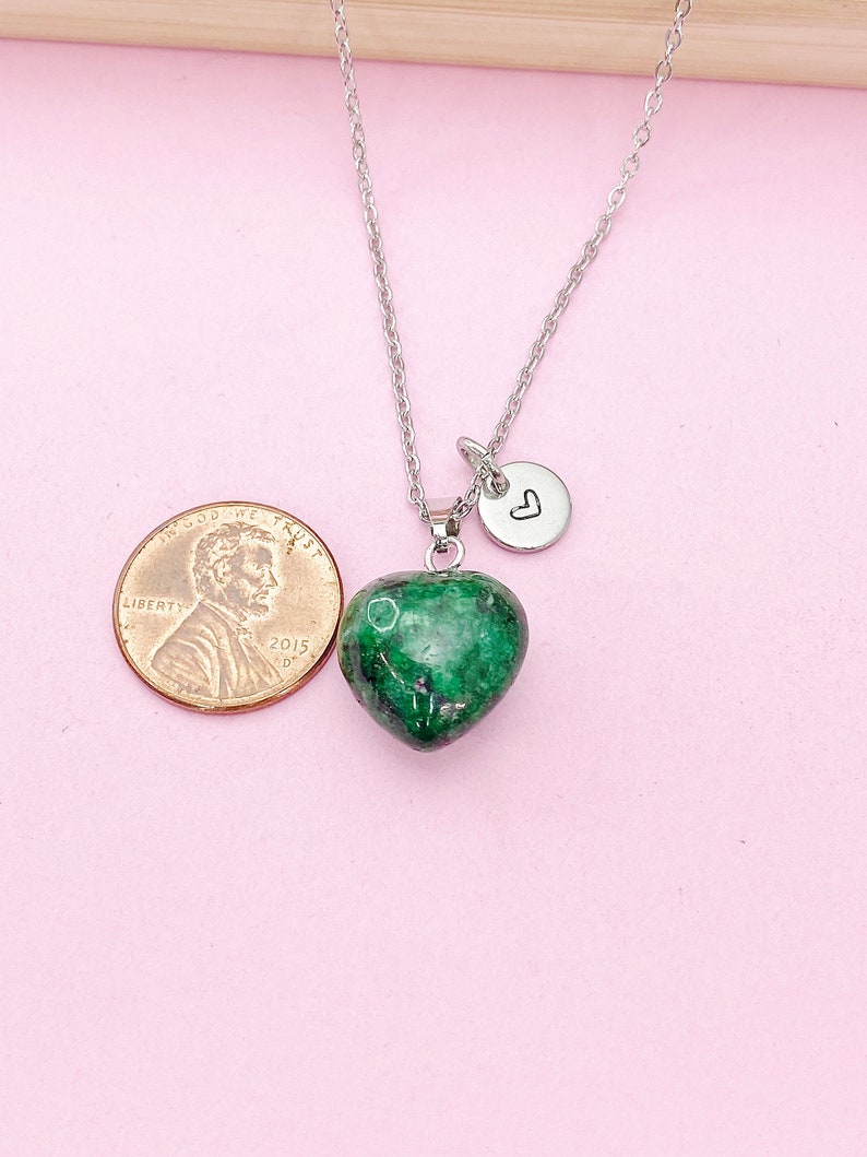 May include: A silver chain necklace with a green heart-shaped pendant and a small silver charm with a heart engraved on it. The pendant is about the size of a US penny.