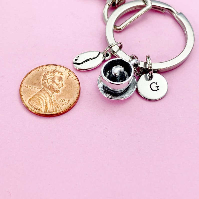 May include: Silver charm keychain with a coffee cup, coffee bean, and a letter G charm. The keychain is attached to a silver key ring. A penny is in the background.