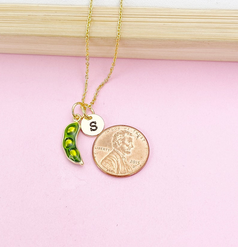Peut inclure: Un collier dor&eacute; avec un charm en forme de cosse de pois et un petit charm rond avec la lettre "S". La cosse de pois est verte avec des pois jaunes &agrave; l'int&eacute;rieur. Une pi&egrave;ce de monnaie est &agrave; c&ocirc;t&eacute; du collier pour la comparaison de taille.