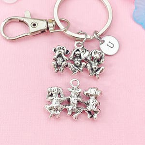May include: Silver-toned keychain featuring three wise monkeys, each in a different pose, and a charm with the letter "U". The keychain also includes a lobster clasp and a split ring for attaching keys.
