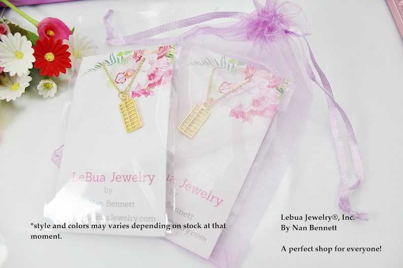 K&ouml;nnte beinhalten: Zwei goldene Abakus-Halsketten auf wei&szlig;en Karten mit Blumenmustern. Die Karten tragen den Text "LeBua Jewelry by Nan Bennett" und "Lebua Jewelry&reg;, Inc. By Nan Bennett. A perfect shop for everyone!"